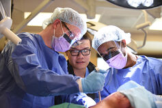 A surgical student observes two surgeons performing a procedure.